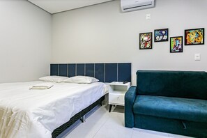Una habitación de hotel con una cama, una mesita de noche, un sofá verde azulado y cuatro cuadros en la pared.