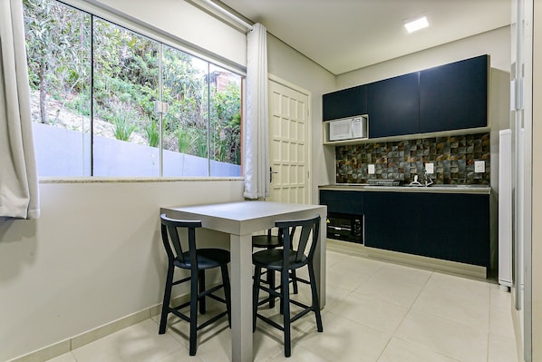 A compact kitchen with a dining area, a window with curtains, and a view of greenery outside. - Decorated Studio Facing the Lagoon Sdr009 (Florianópolis)
