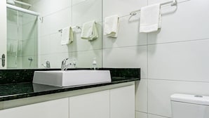 Un baño moderno con azulejos blancos, encimera negra, lavabo blanco, espejo y retrete.