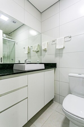 Un baño moderno con azulejos blancos, encimera negra, lavabo blanco, espejo y retrete.