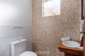 Ein Badezimmer mit Wand aus Mosaikfliesen, einer weißen Toilette und einem Holzwaschtisch.