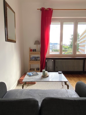 A room with a window, a radiator, a table with a book, a lamp, and a red curtain. - Beautiful apartment just a stone's throw from downtown, with a parking space (Blois)