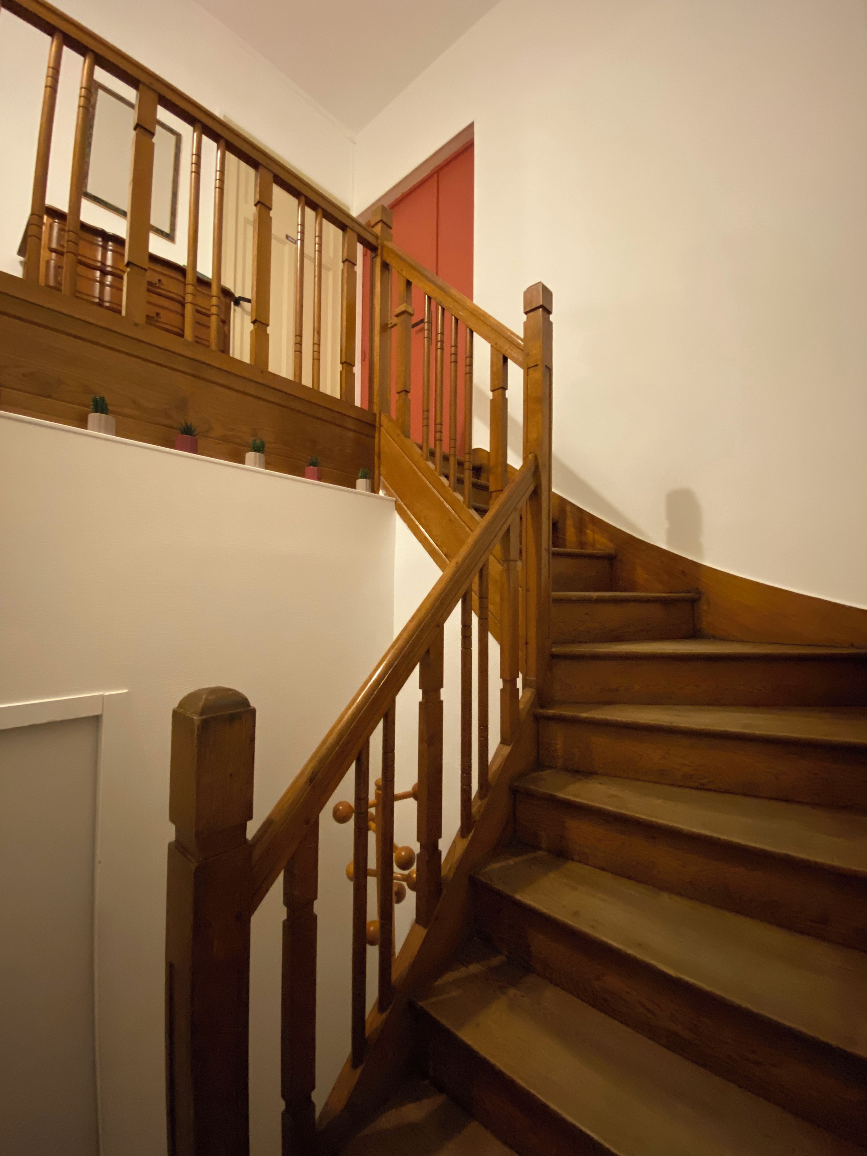 Un escalier en bois avec une rampe et une porte rouge en haut.