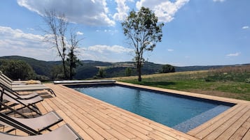 Une terrasse en bois avec des chaises longues et une piscine.
