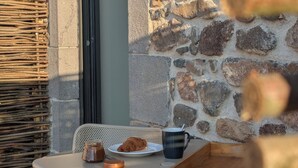 Taula amb un plat de menjar, una tassa i un bocal, davant d'una paret de pedra.