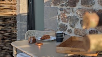 Une table avec une assiette de nourriture, une tasse et un bocal, le tout placé devant un mur de pierres.
