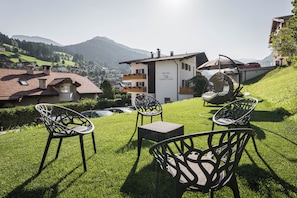 A hotel with a white exterior, a balcony with wooden railings, and a hanging chair in the garden. - Garni Toni (Ortisei)