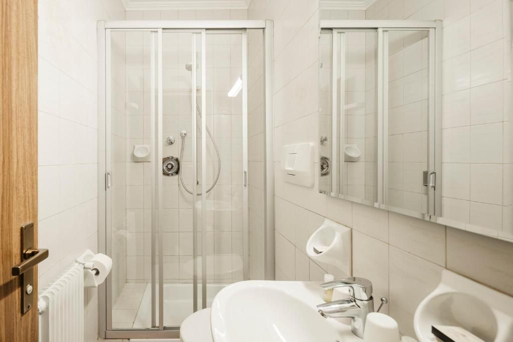 Ein modernes Badezimmer mit einer Glaskabine zur Dusche, einem weißen Waschbecken und einem Spiegel darüber.