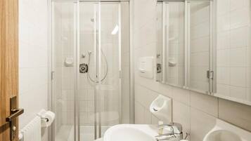 Un baño moderno con ducha envuelta en vidrio, un lavabo blanco y un espejo sobre el lavabo.