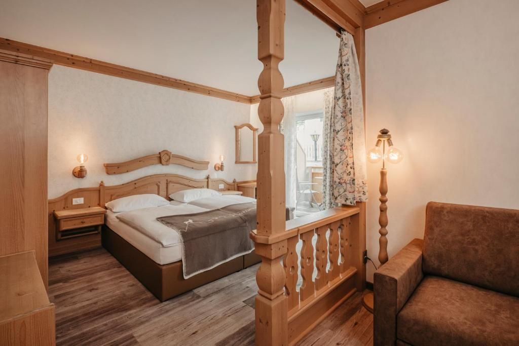 Un dormitorio con una cama con dosel de madera, una mesita de noche, una silla y un ventanal con cortinas.