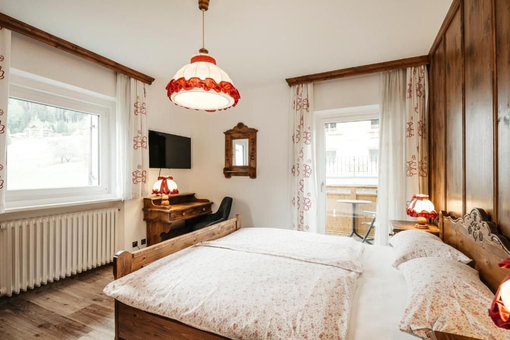 Una camera da letto con un letto grande, una scrivania in legno, una sedia, un televisore e una finestra con tende.
