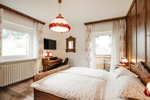 Quarto com cama grande, escrivaninha de madeira, cadeira, televisão e janela com cortinas.