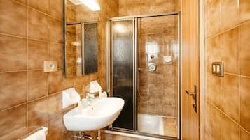 Un baño con un lavamanos blanco, cabina de ducha con vidrio y un espejo.