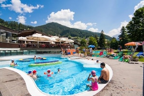 Un espace piscine où des personnes nagent et s’amusent, entouré de chaises longues et de parasols.