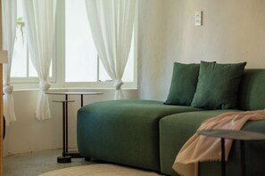 A green sofa with two pillows, a small round table, and a window with sheer curtains. - SEN House Hoi An - 2 Bedrooms with Pool, Kitchen and Rooftop (Hoi An Tay)