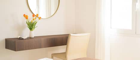 A hotel room with a bed, a chair, a bedside table with a vase of flowers, and a mirror on the wall.
