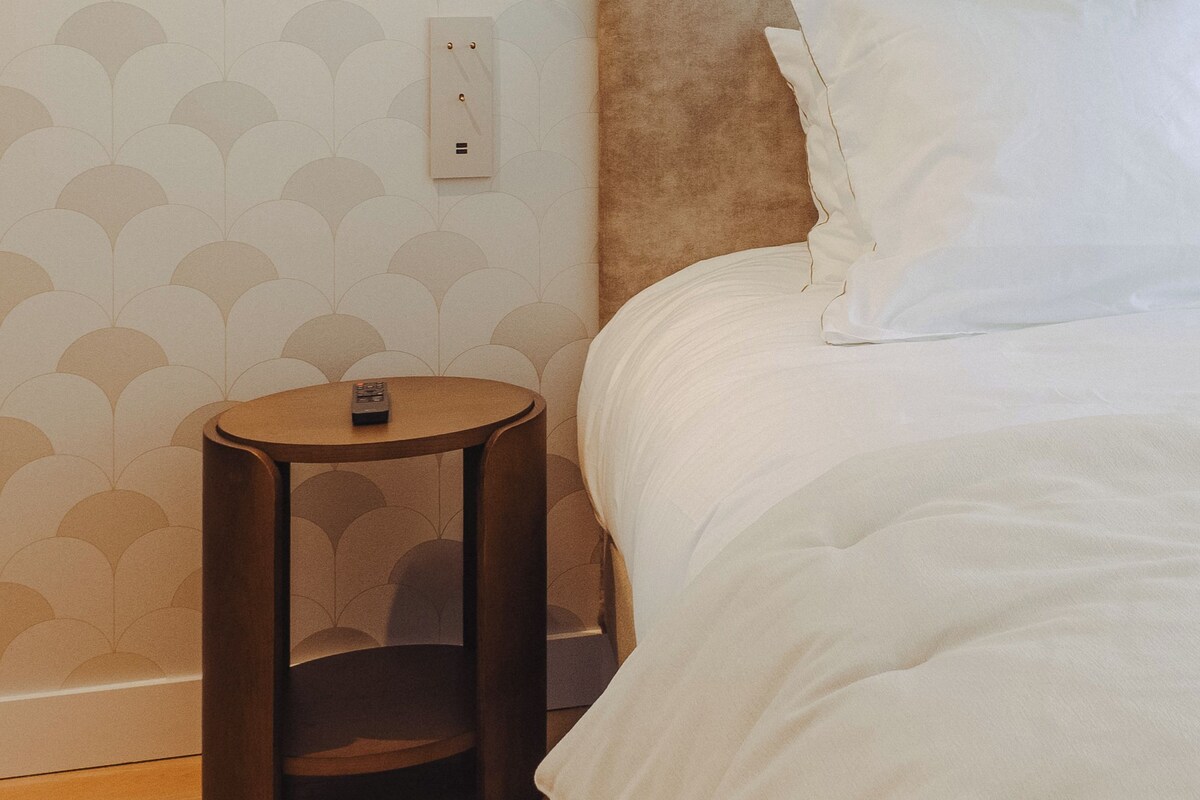 Ein Hotelzimmer mit einem Bett, einem runden Nachttisch, einer Steckdose und einer Wandleuchte.
