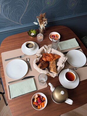 Ein Frühstückstisch mit Holzoberfläche, einer Obstschale, einem Croissant, einer Teekanne und einer Tasse Tee.