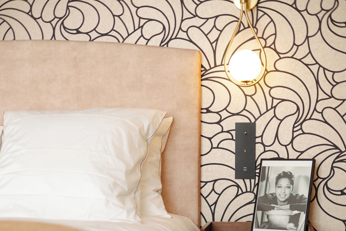 Ein Bett mit Kopfteil, ein Nachttisch mit Lampe und ein gerahmtes Foto darauf.