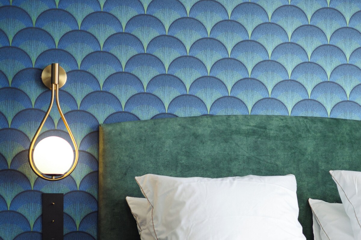 Ein Bett mit weißen Laken, einem grünen Kopfteil und einer Wand mit blauem Muster.