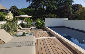 Ein Poolbereich auf dem Dach mit Holzterrasse, Liegestühlen und einem kleinen Tisch mit Sonnenschirm.