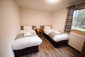 A room with two beds, a nightstand, and a window with curtains. - Sidlaw (Dundee)