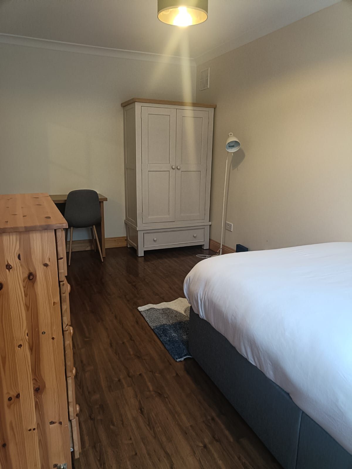 A bedroom with a bed, a wooden dresser, a desk with a chair, and a wardrobe.
