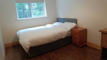 A bedroom with a bed, a nightstand, a window, and a wooden floor.