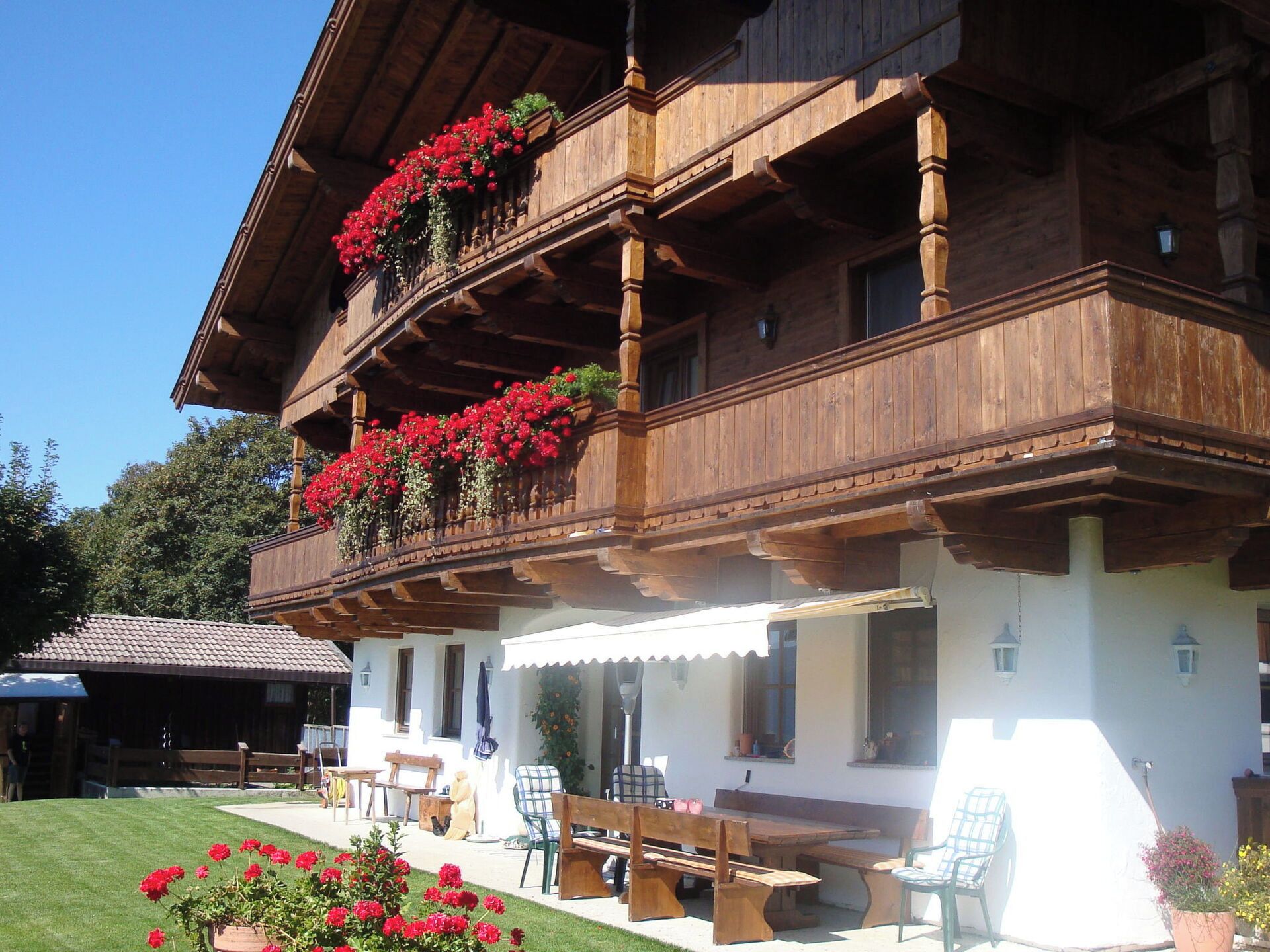 A traditional wooden chalet with a balcony adorned with red flowers, outdoor seating, and a well-maintained lawn.