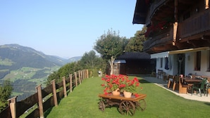 A wooden fence, a table with a flower pot, and a building with a balcony. - Lovely apartment for 4 people with WIFI, TV and balcony (Hopfgarten Im Brixental)