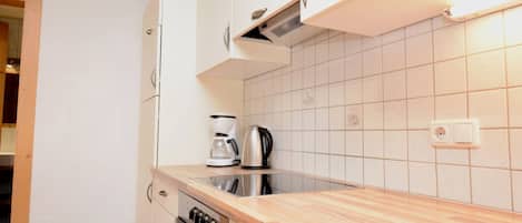 A kitchen with white cabinets, a wooden countertop, a coffee maker, and a kettle.