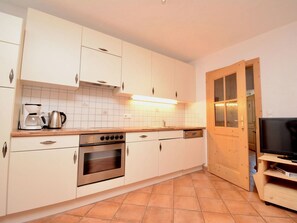 Eine moderne Küche mit weißen Schränken, einem eingebauten Ofen, einer Kaffeemaschine und einem Fernseher auf einem Holzboden.