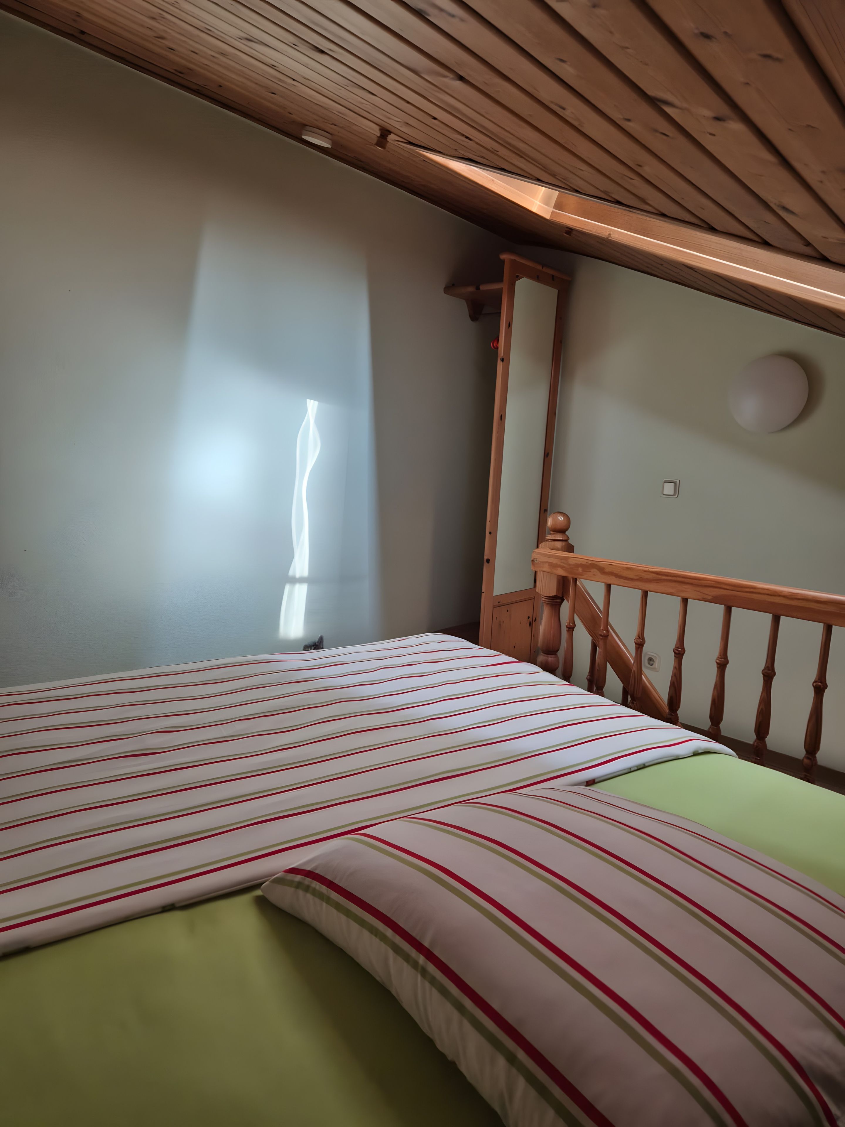 Une pièce avec un lit, un plafond en bois, un luminaire et un interrupteur mural.