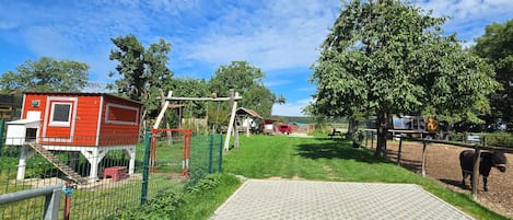 A fenced outdoor area with a red building, a wooden structure, and a black animal.