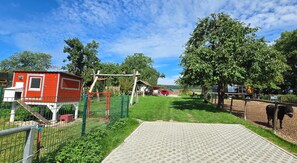 Un espacio exterior cercado con un edificio rojo, una estructura de madera y un animal negro.