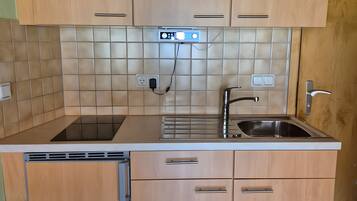 Een kleine keuken met houten kastjes, een ingebouwde vaatwasser, een roestvrijstalen spoelbak en een betegelde spatwand.