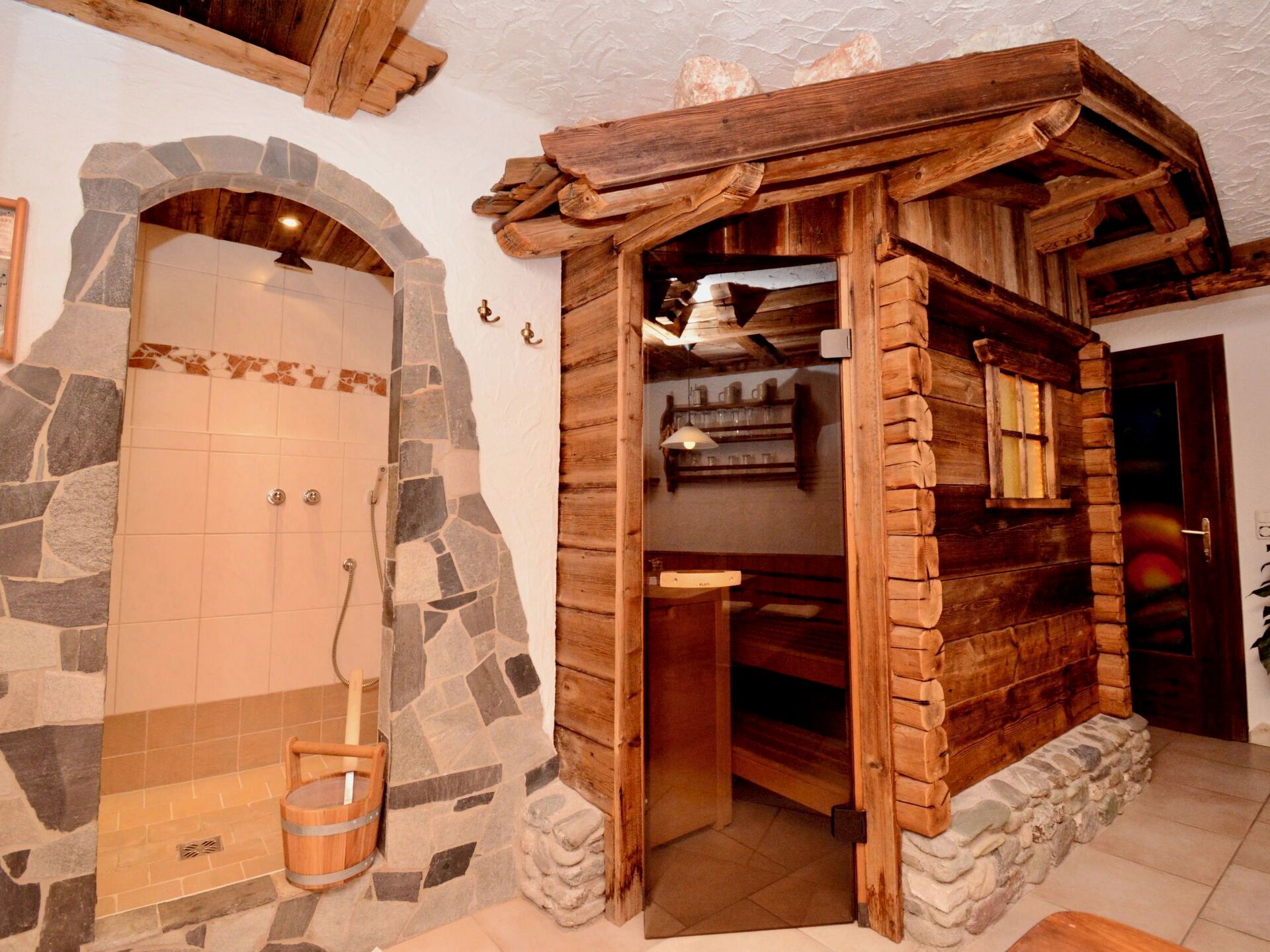 Een douchegedeelte met stenen tegels, een houten deur en een houten boog die leidt naar een kamer met planken.