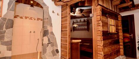 Zona de ducha con suelo de baldosas de piedra, una puerta y un arco de madera que dan a una habitación con estantes.