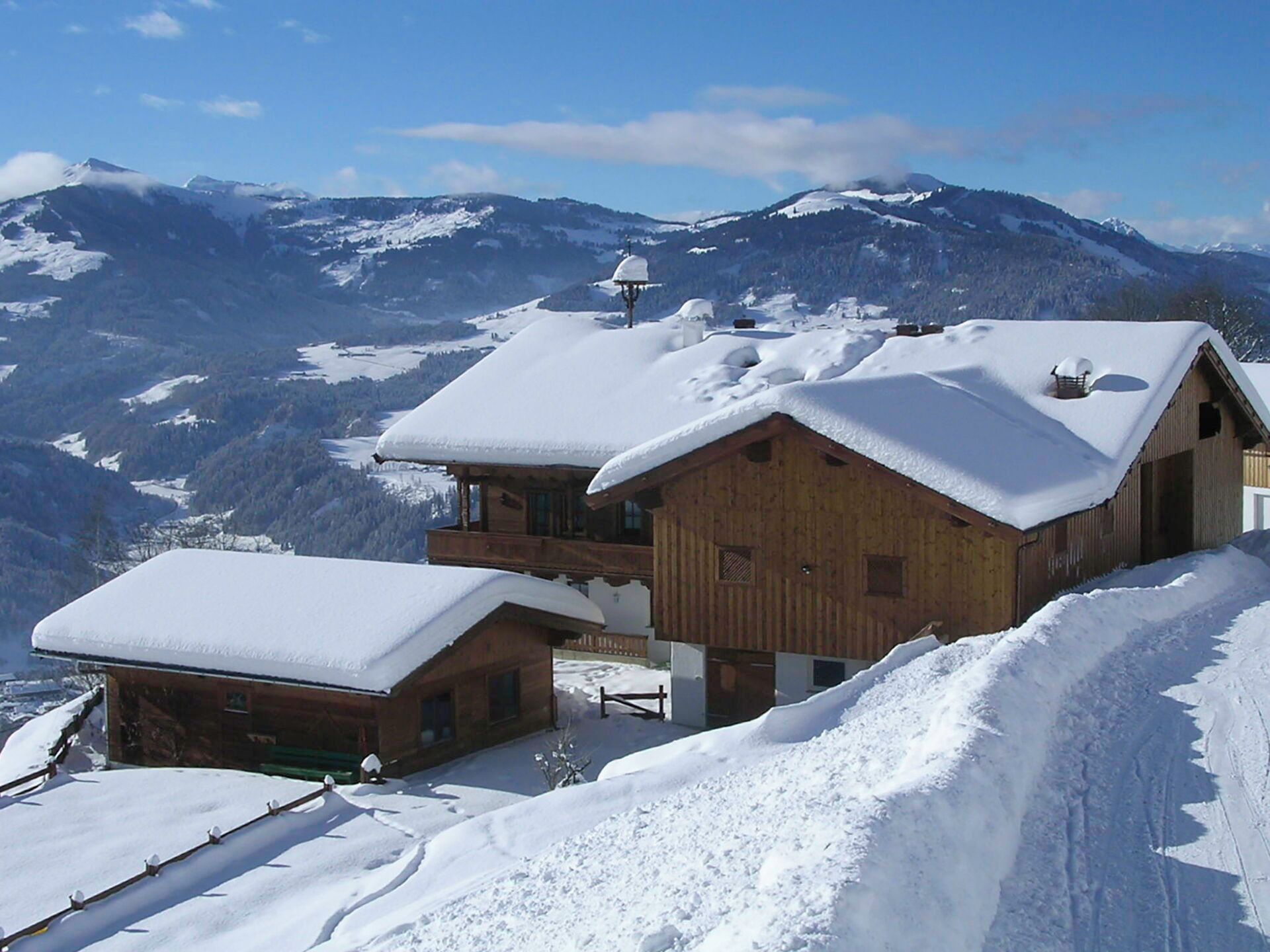 Una cabaña de madera con balcón, rodeada de montañas nevadas y cielos despejados.
