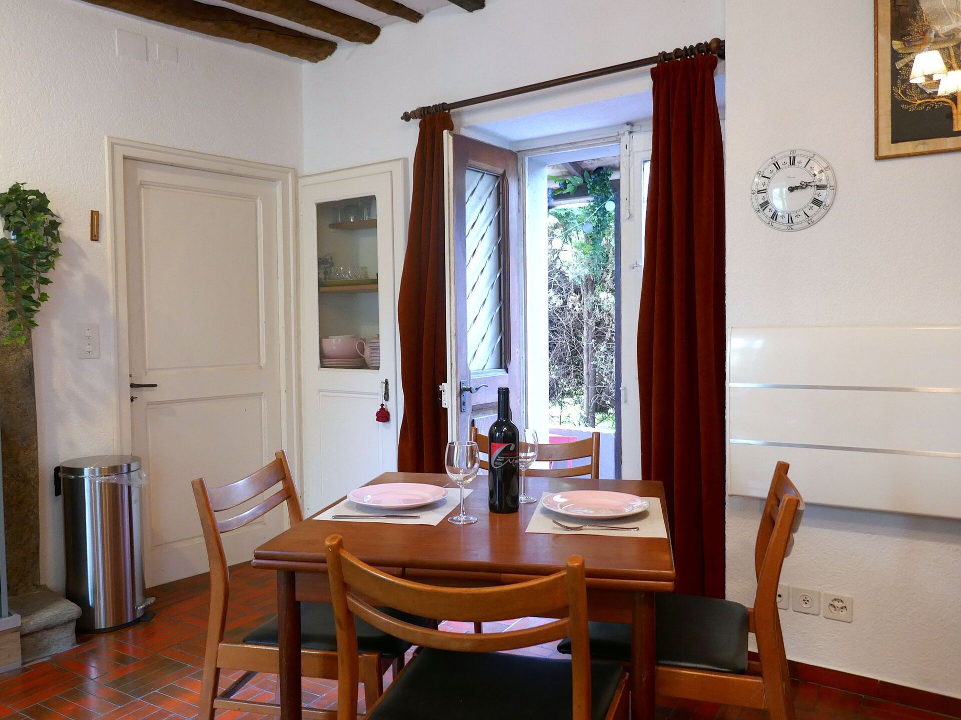 Un coin repas avec une table en bois, des chaises, une bouteille de vin et une horloge au mur.