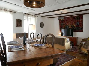 Un comedor con una mesa de madera dispuesta para una comida, un televisor sobre un mueble y un tapiz en la pared.