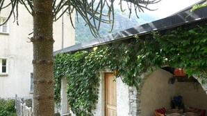 A rustic outdoor seating area with stone walls and a wooden door, surrounded by greenery and a mountain backdrop. - Lovely apartment for 4 people with WIFI, TV, balcony and panoramic view (Acquarossa)