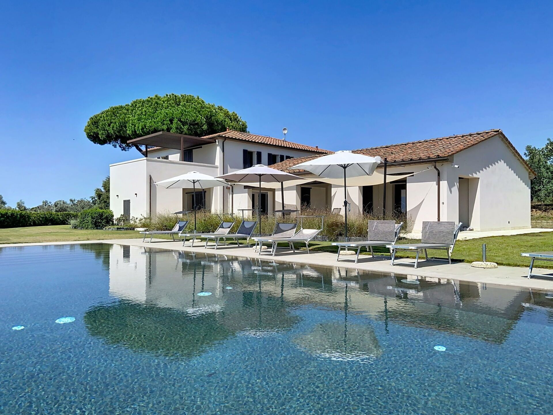 A modern villa with a swimming pool, sun loungers, and umbrellas.