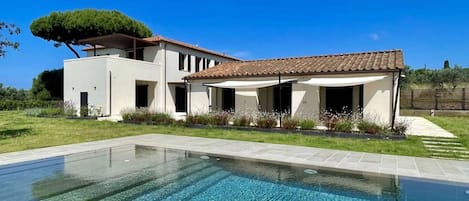 Una casa moderna con piscina, terraza cubierta y césped bien cuidado.
