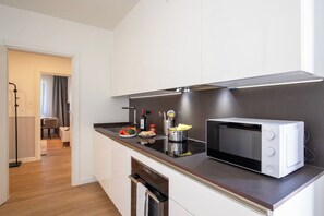 A modern kitchen with a microwave, a stove, and a sink. There is a dining area visible in the background. - Boutique Suites Two Bedroom Apartment with AC (Lugano)