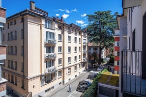 A multi-story residential building with balconies, a clear sky, and parked cars on the street. - Boutique Suites Two Bedroom Apartment with AC (Lugano)