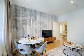 Ein zeitgemäßer Essbereich mit rundem Tisch, Stühlen, einem Fernseher und einem kleinen Tisch mit einer Essplatte.