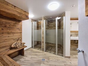 Une salle de bain moderne avec un mur en bois, une cabine de douche en verre et un banc muni d’un panier.