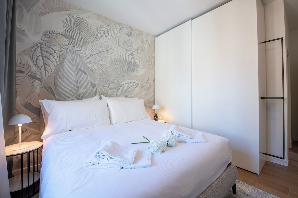 Una habitación de hotel con una cama grande, una mesita de noche con una lámpara y una pared con diseño de hojas.
