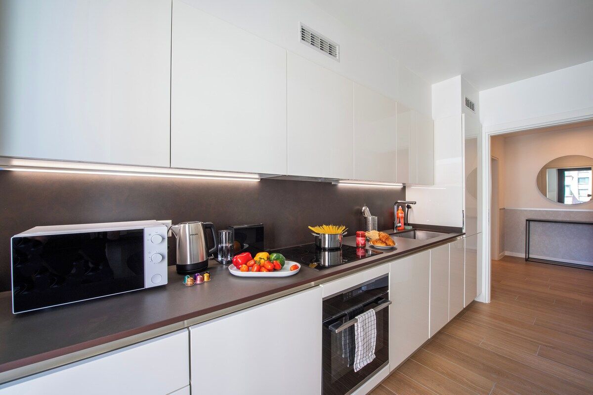 A modern kitchen with white cabinetry, a built-in oven, a microwave, and a stainless steel sink.